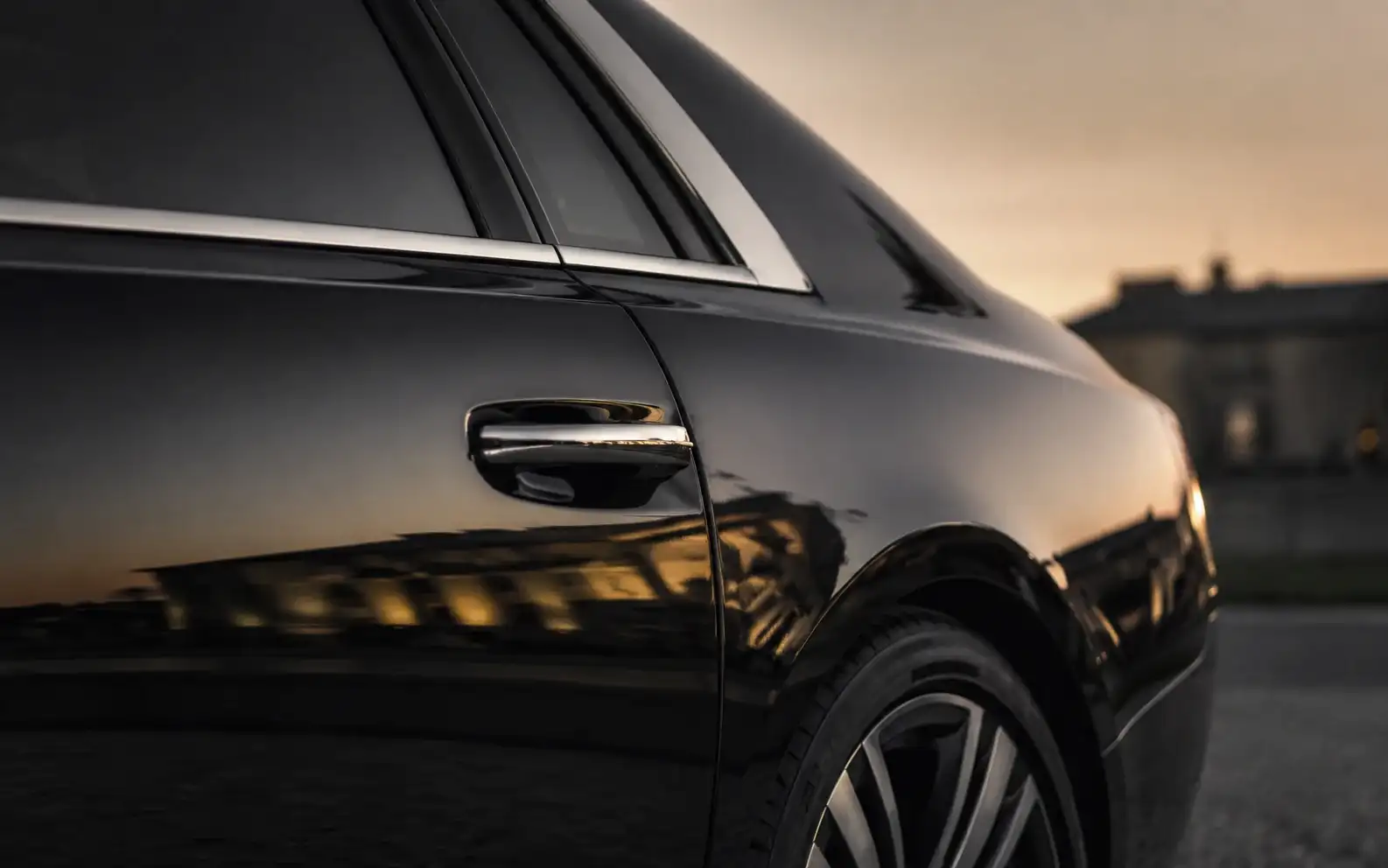 The rear quarter of a black ultra-luxury saloon at dusk, with a warm reflection along the flank.